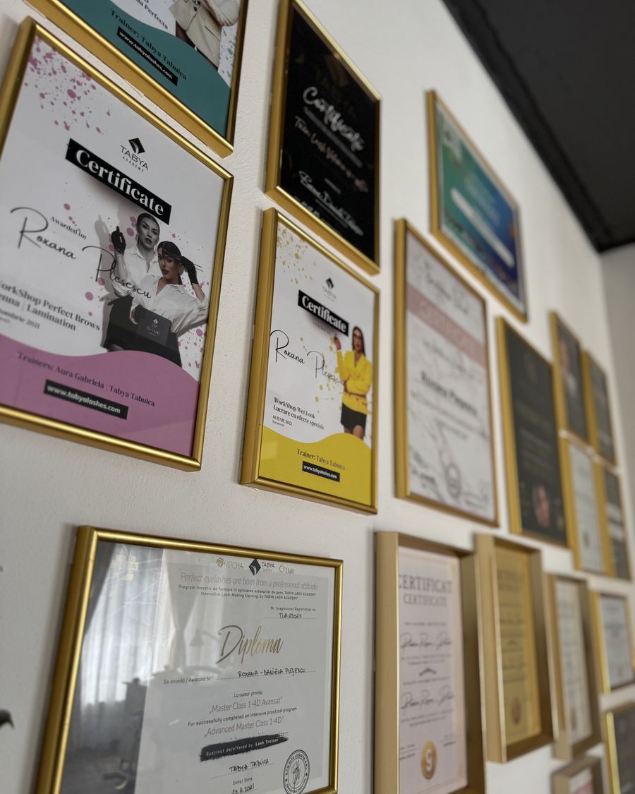 Peretele cu diplomele Roxanei Pleșescu, în rame aurii: certificate Tabya Academy pentru gene și sprâncene, diplome de manichiură și machiaj.