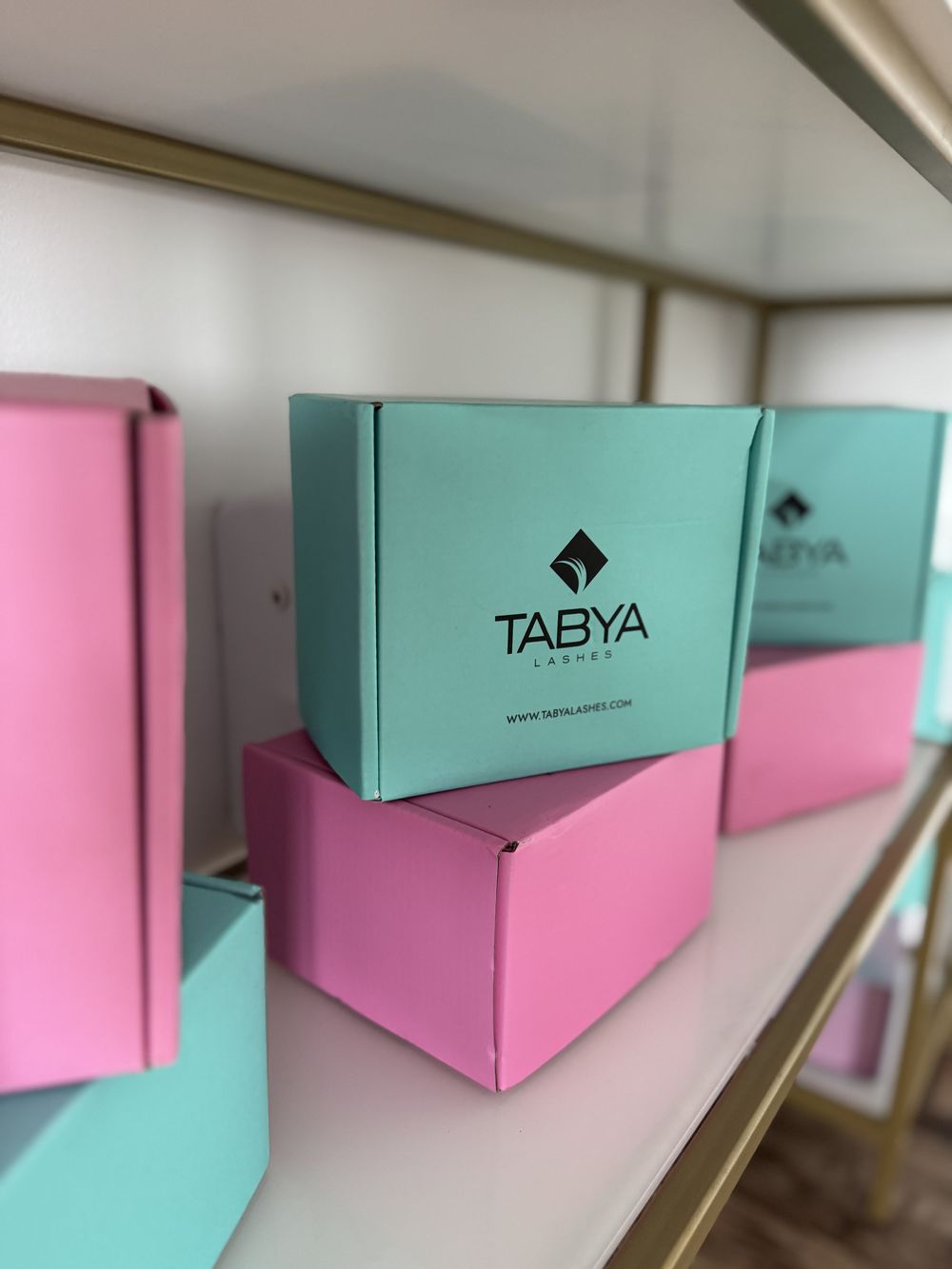 Cutii Tabya Lashes pe raftul auriu al salonului.