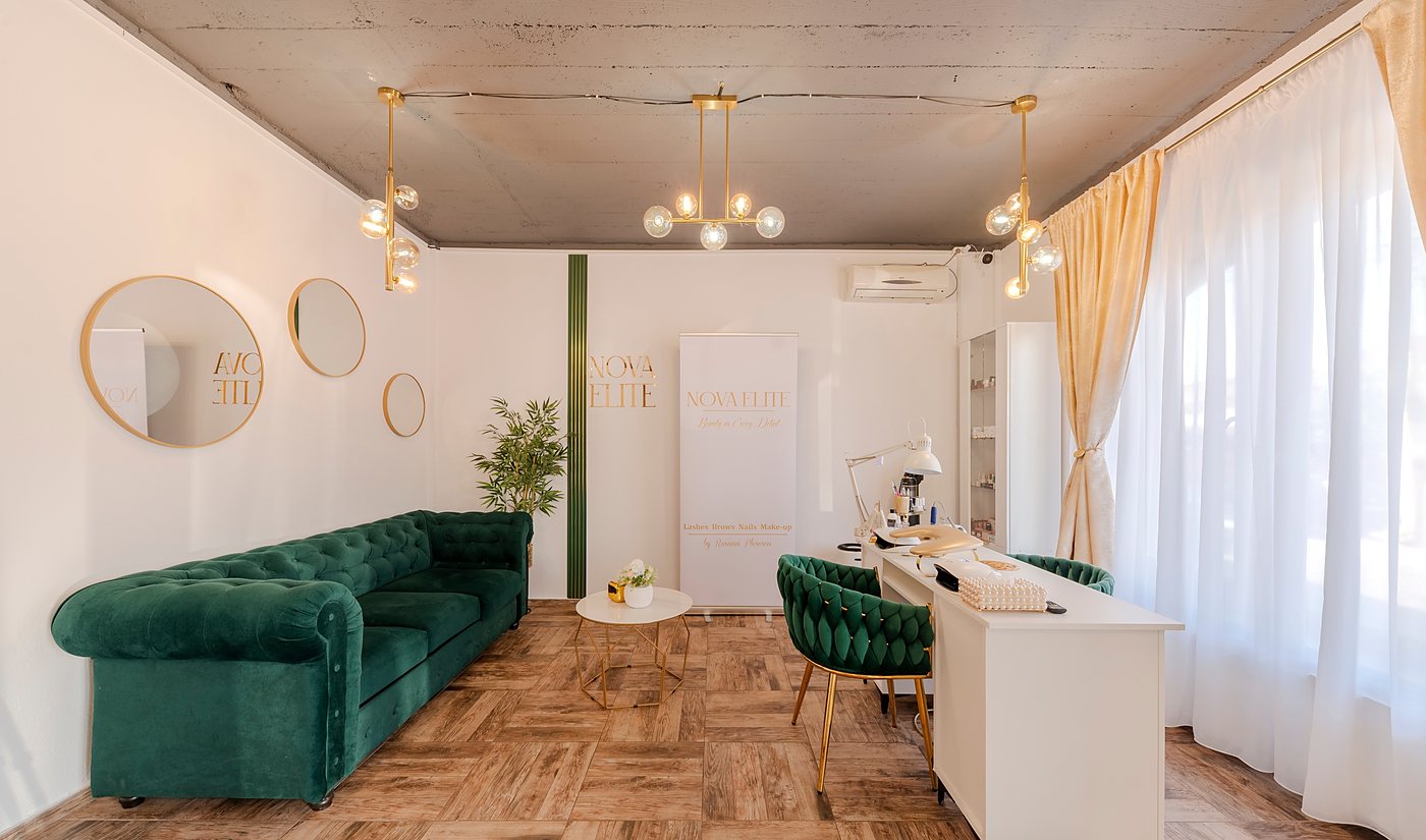Zona de așteptare: canapea Chesterfield din catifea verde, oglinzi rotunde aurii și logotipul în relief pe peretele cu lamele verzi.